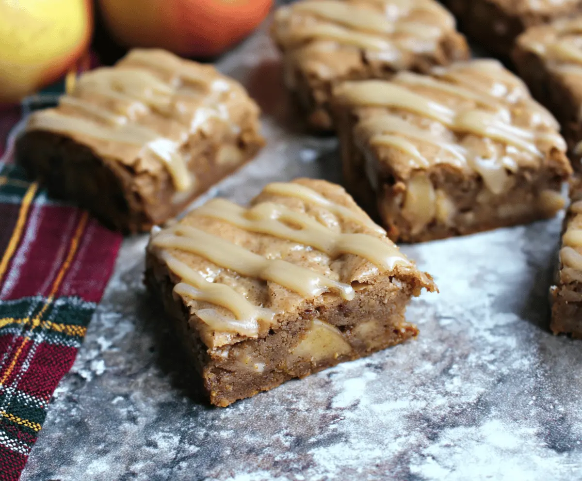 Delicious homemade apple brownies topped with a glossy maple glaze on a rustic wooden table, showcasing a flavorful apple-infused dessert with sweet caramel tones.