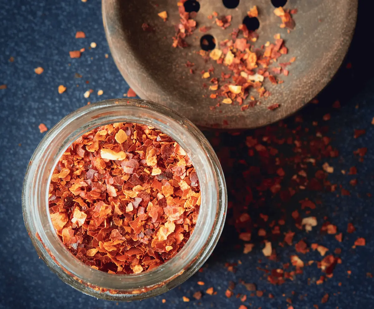 Homemade chili flakes in a glass jar with a spoon, ready to add spicy flavor to dishes