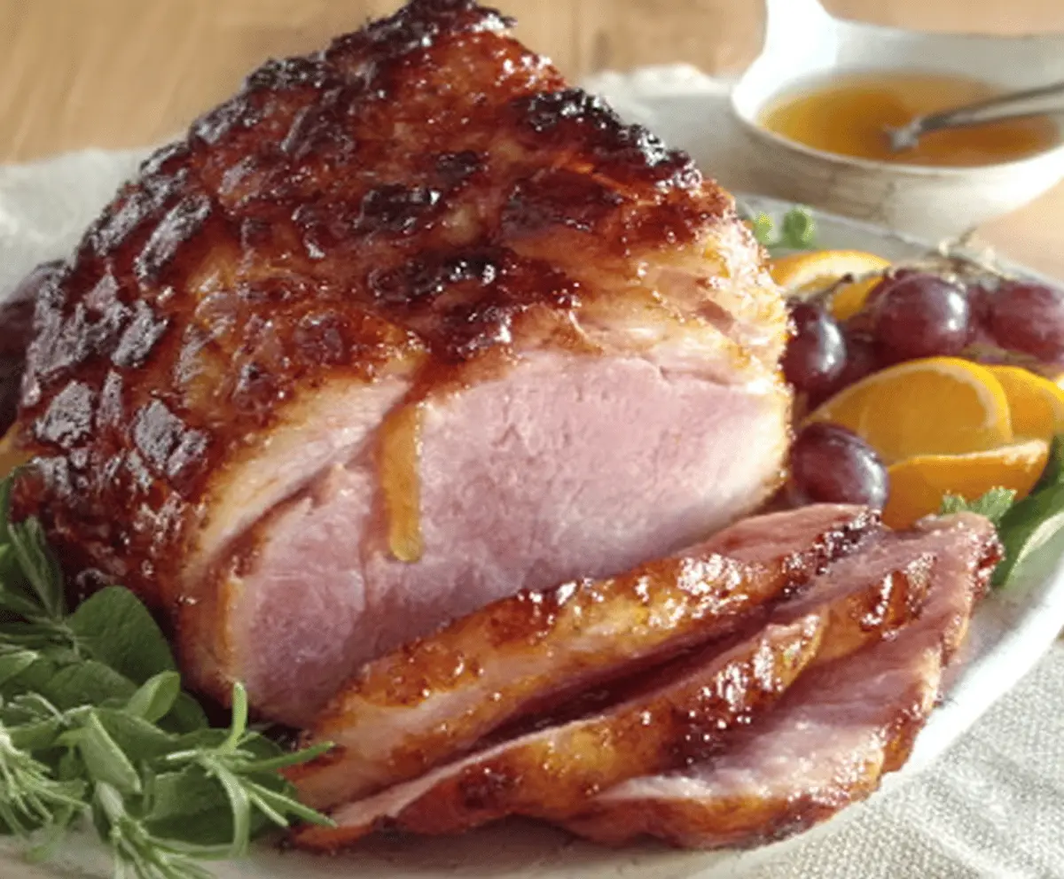 Delicious maple-glazed ham garnished with fresh herbs on a rustic wooden platter, perfect for holiday dinners