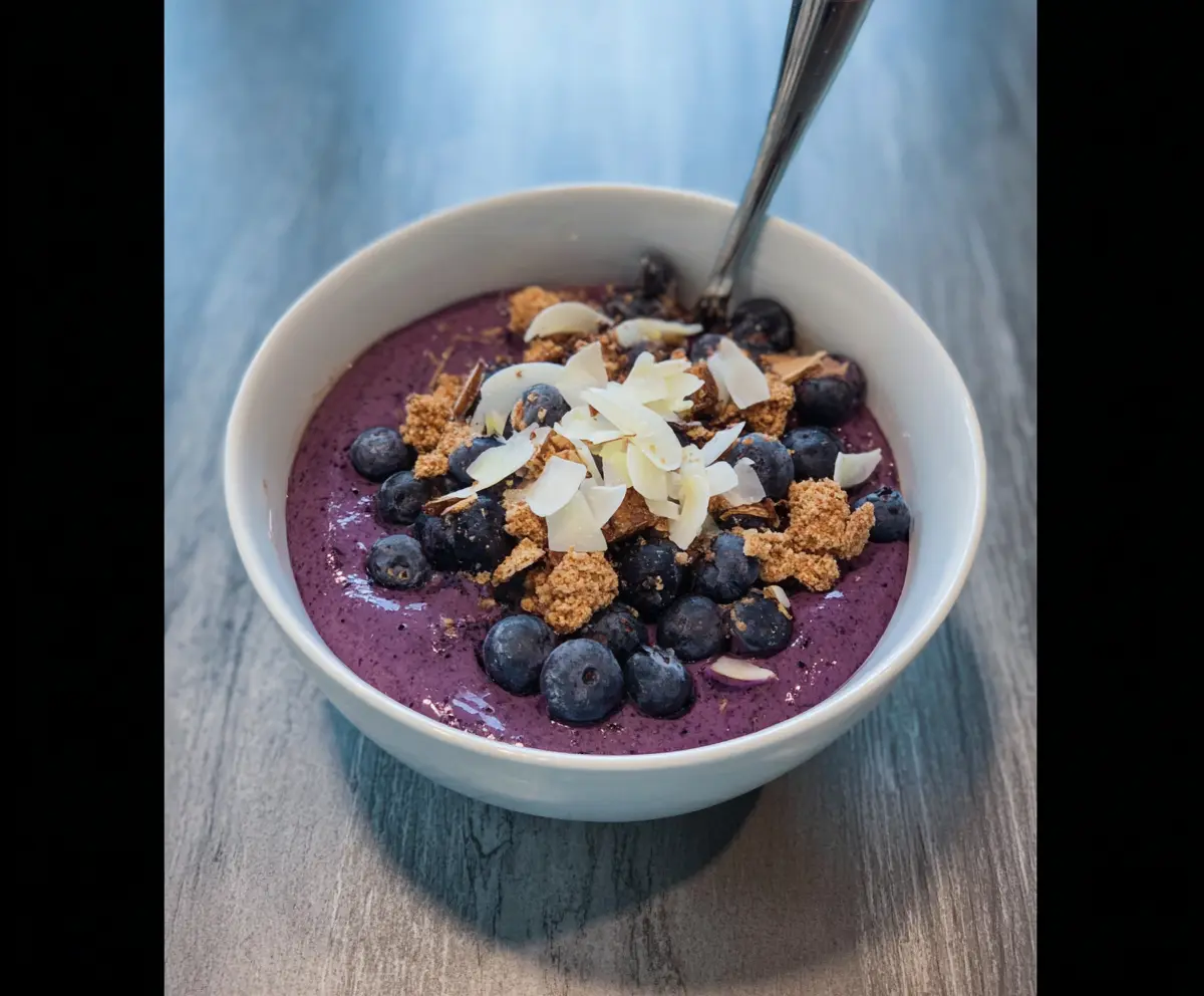 Vibrant blueberry smoothie bowl topped with fresh blueberries, sliced bananas, and granola for a healthy breakfast.